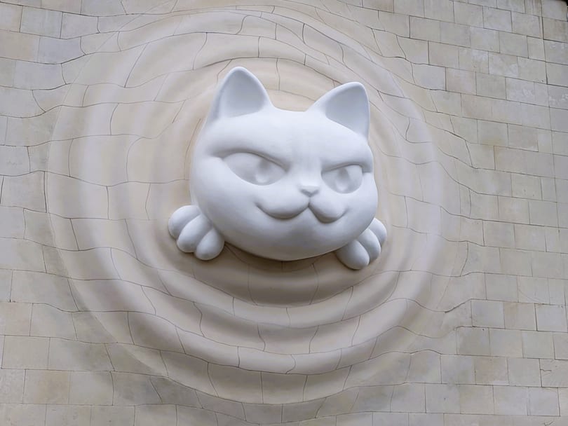 A large white cat sculpture pushing head first out of the tiled wall of pavilion 9 at VDNH